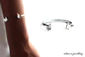 Silver butterfly bangle on a wrist  with another identical  butterfly bangle next to it on a white background