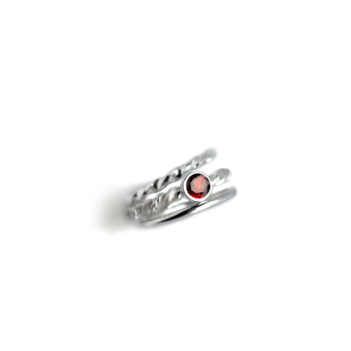3 Silver rings. Middle one with red garnet on white background