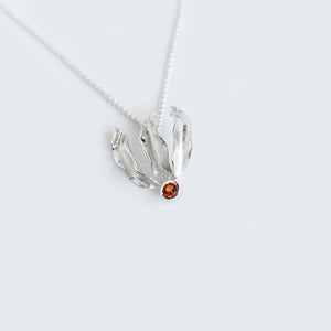 Silver flame lily pendant with garnet gemstone on chain. White background
