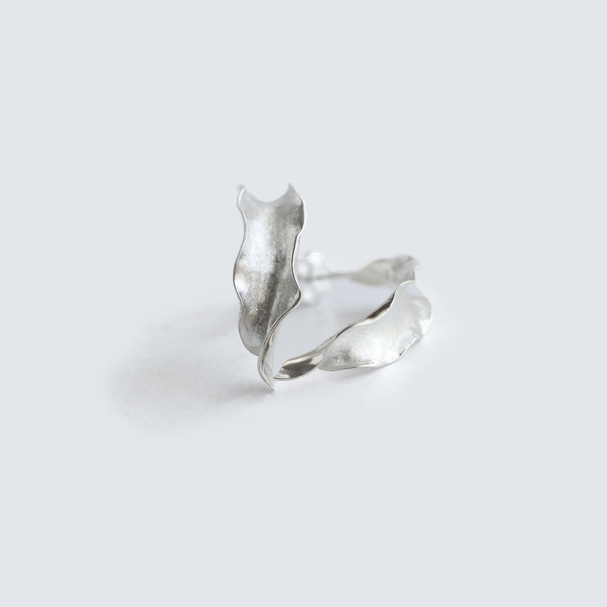 Silver Flame lily petal earrings on soft grey background