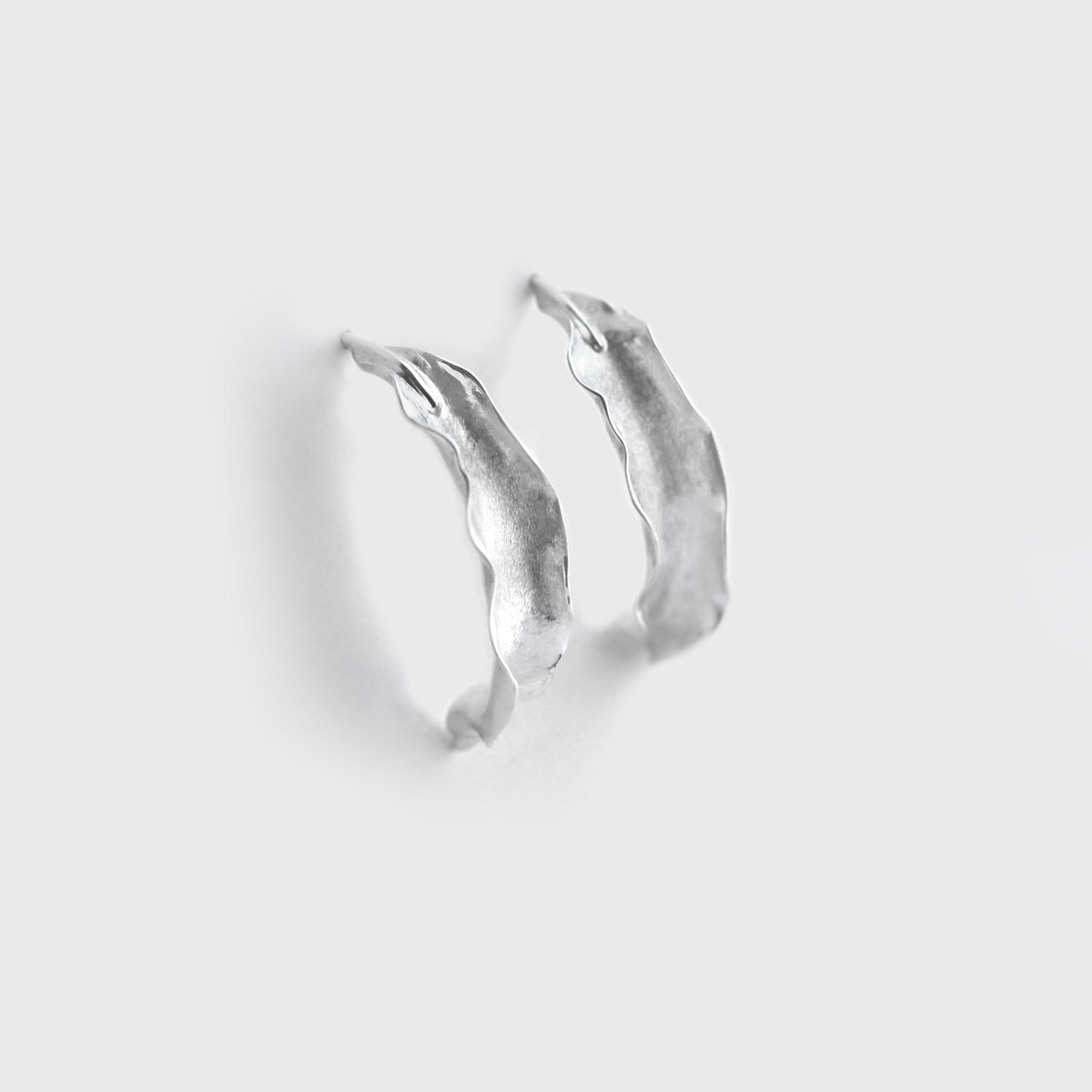 Silver Flame lily petal earrings on soft grey background