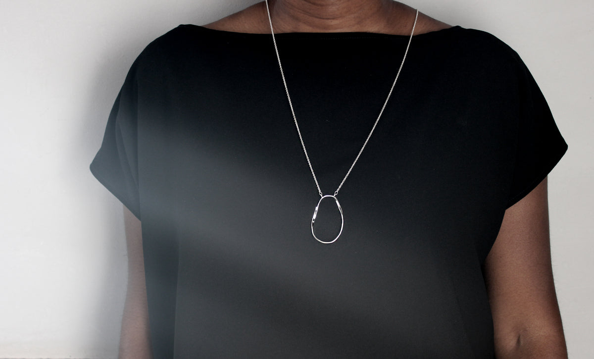 Orb pendant on long chain worn by model in black top.