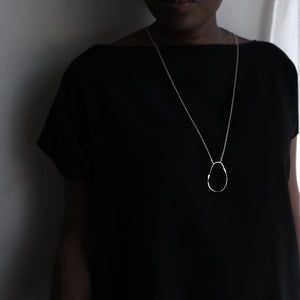 Orb pendant on long chain worn by model in black top.