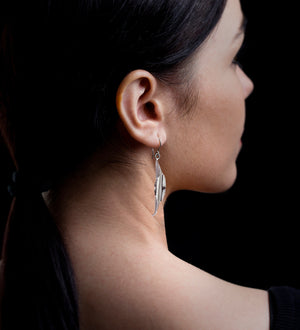 Woman wearing silver leaf earrings, black background 