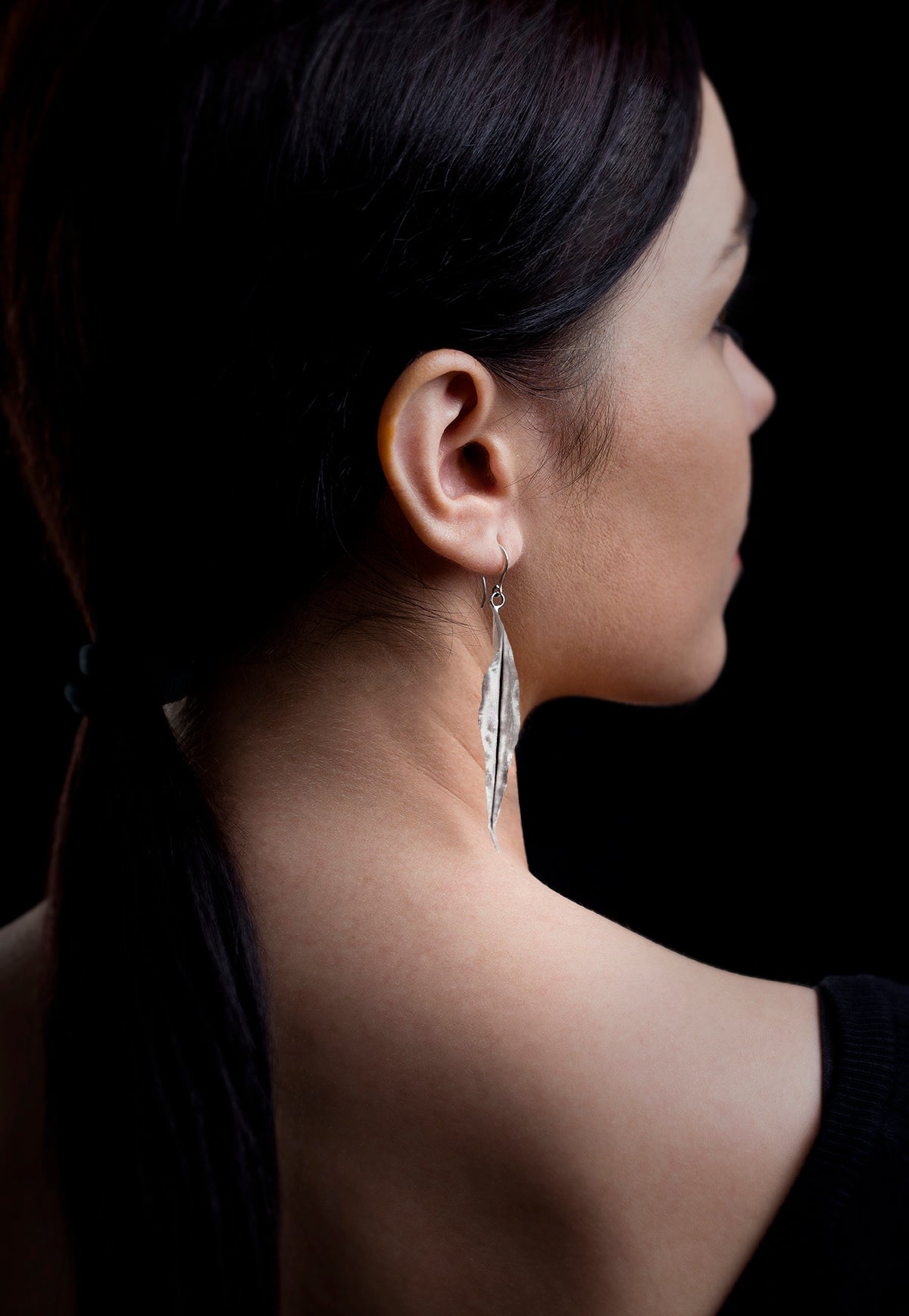 Woman wearing long sterling silver leaf earrings. Black background 